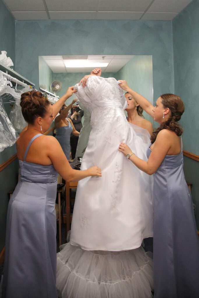 Sarah’s bridesmaids helping her wear her gown