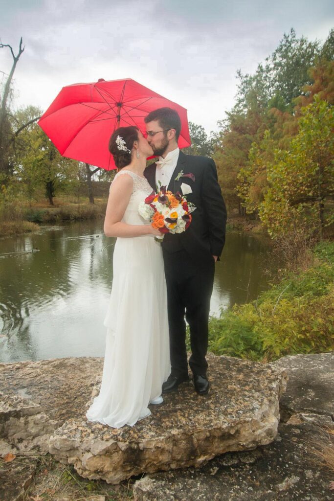 Casey and Joseph kiss under a red umbrella