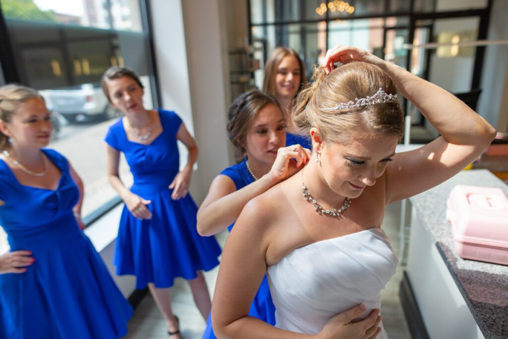 A bridesmaid helping Sarah put on her necklace