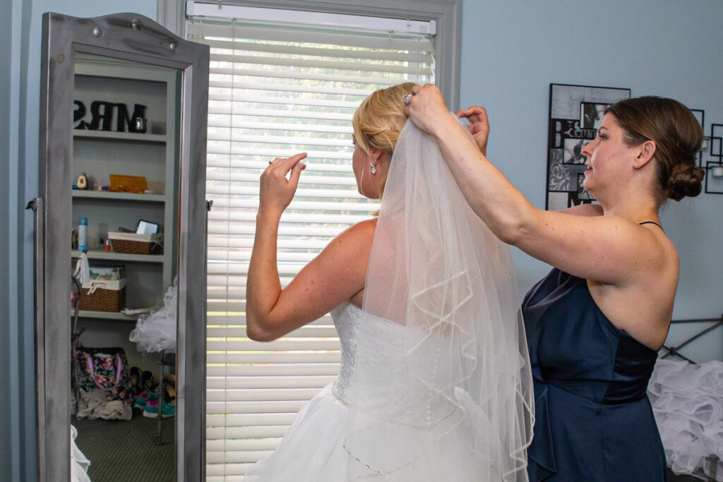 A bridesmaid helping Lindsey put on her wedding veil