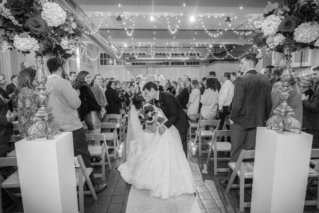 Kelsey and Nick kissing along the aisle grayscaled