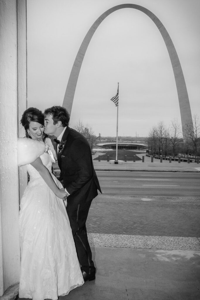Nick kissing Kelsey on the cheek with the Gateway Arch as their background