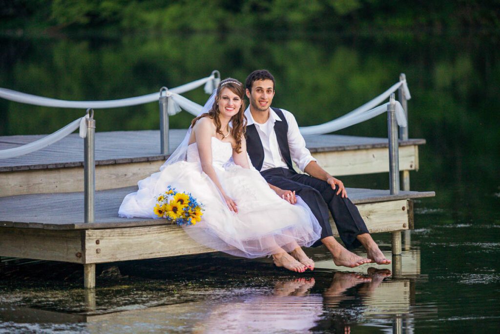 A bride and groom sitting at the edge of a pier