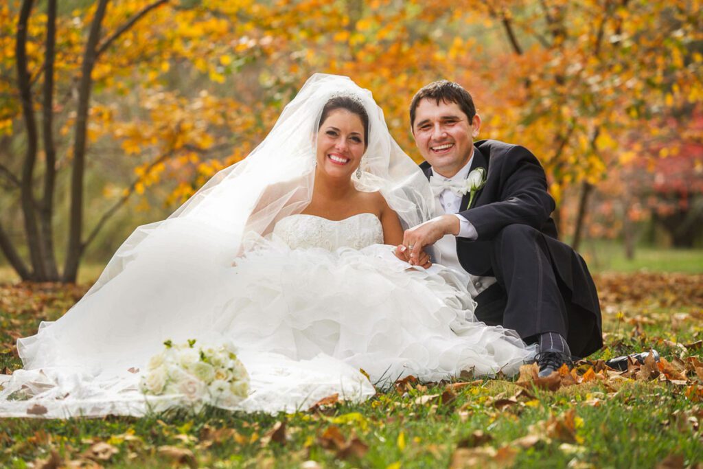 The bride and groom sitting on the grass during autumn