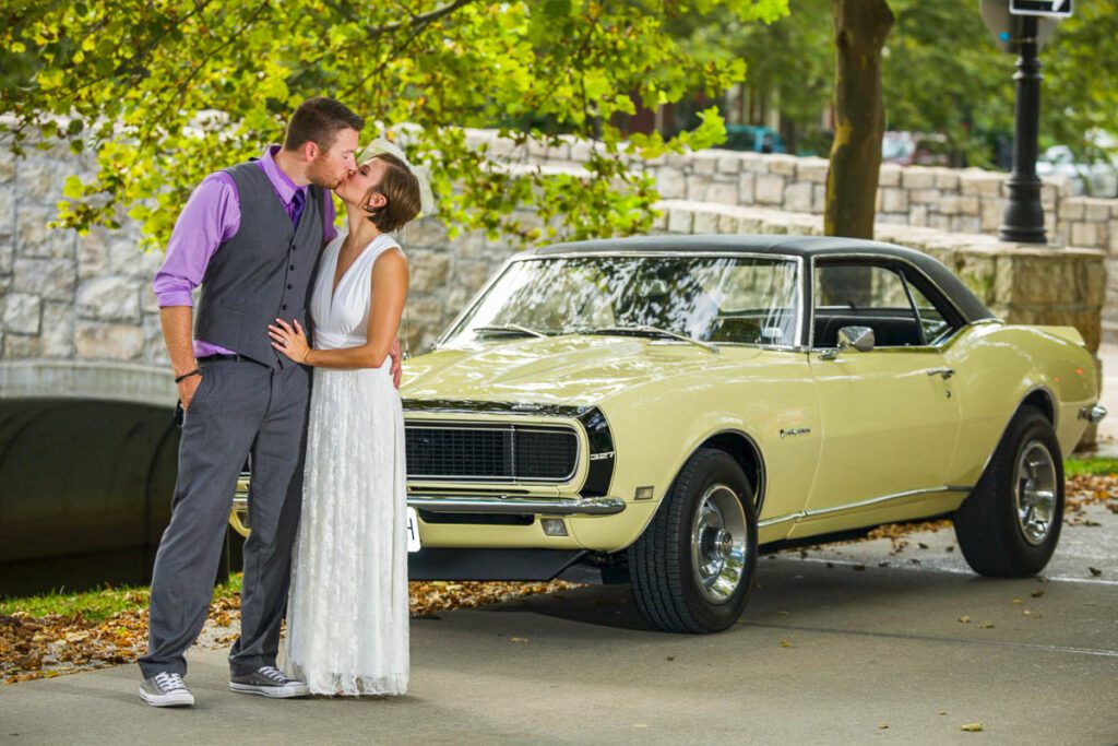 The bride and groom kiss in front of a car