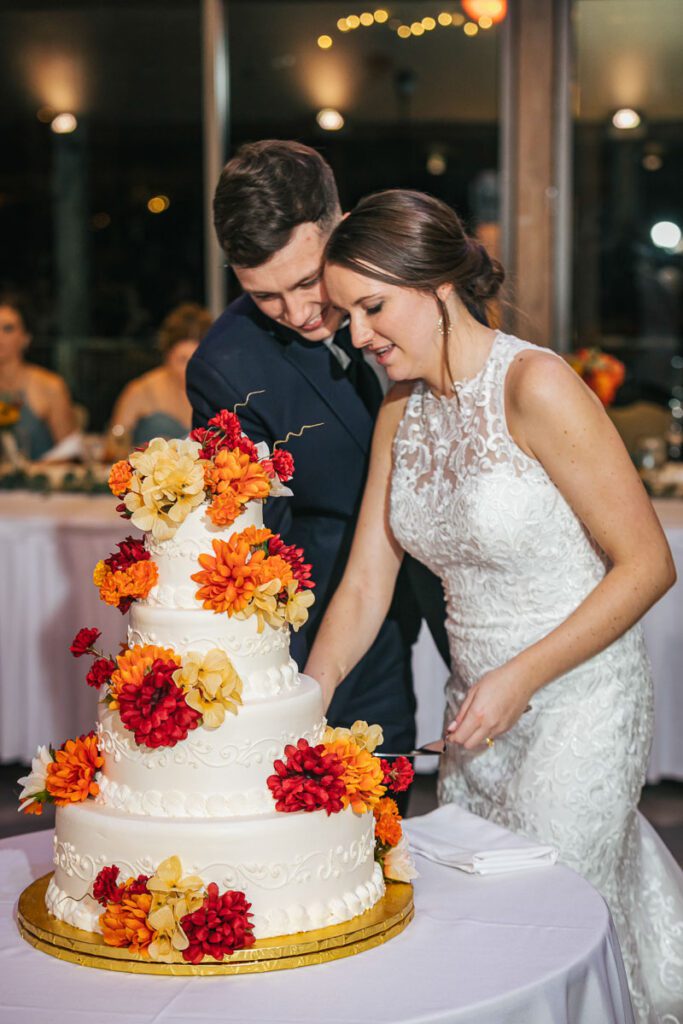 A bride and groom slice their large white wedding cake