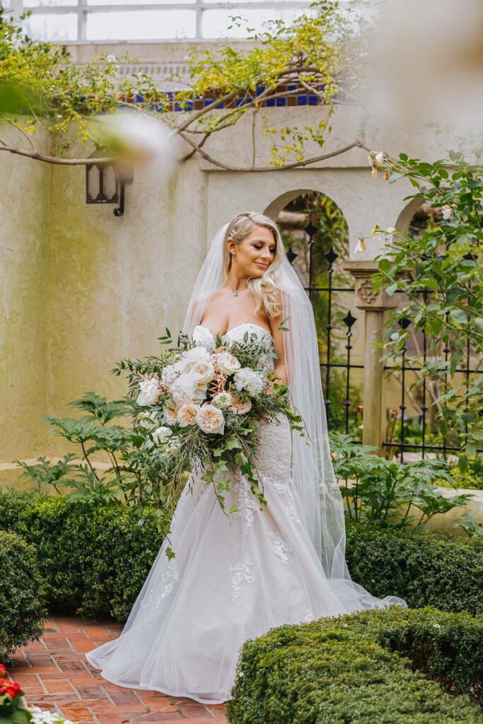 A bride holding a large bouquet of white roses in a garden