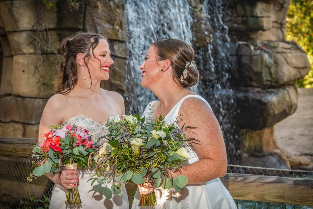 Brides smiling at each other near a waterfall