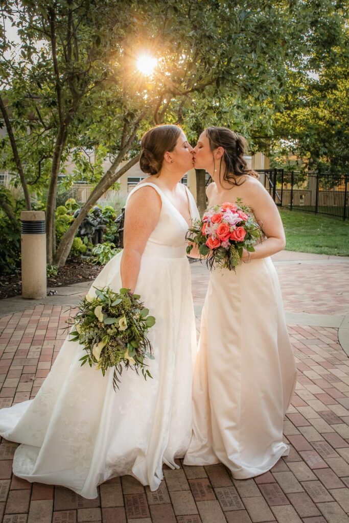 Two brides share a kiss in an afternoon sky