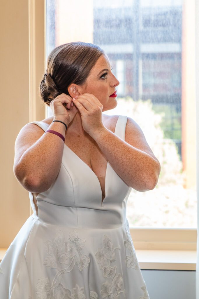 A bride fixing her earring by the window