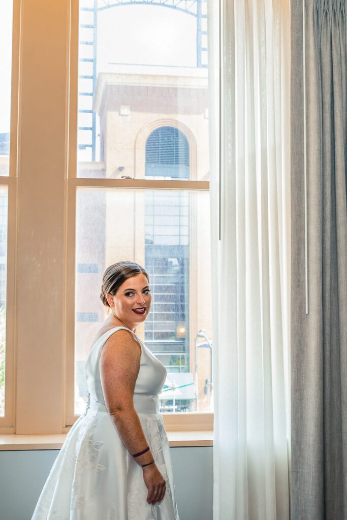 A bride standing by the window in her white wedding dress