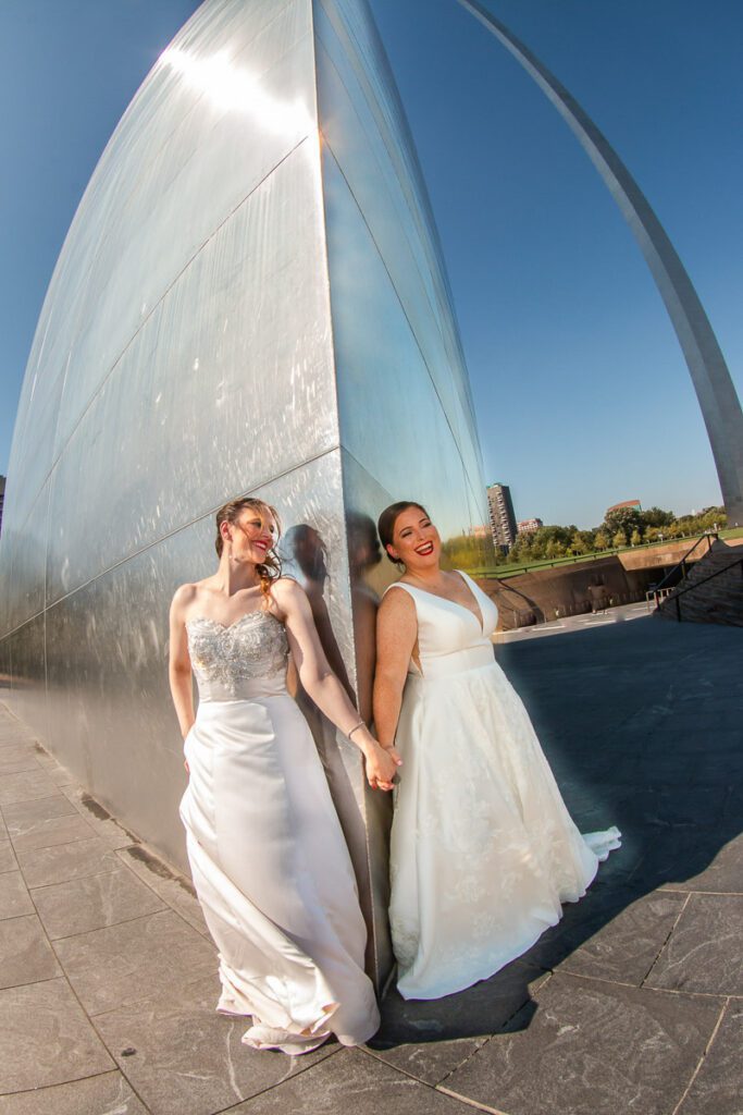 The brides holding hands at the corner of the Gateway Arch