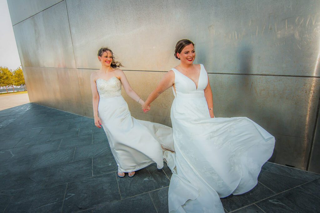 The brides holding hands standing near the Gateway Arch