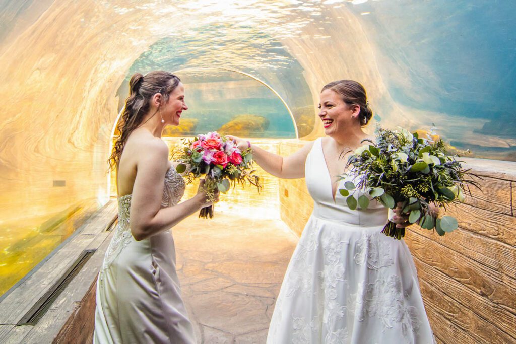 The brides under an ocean aquarium holding their flowers