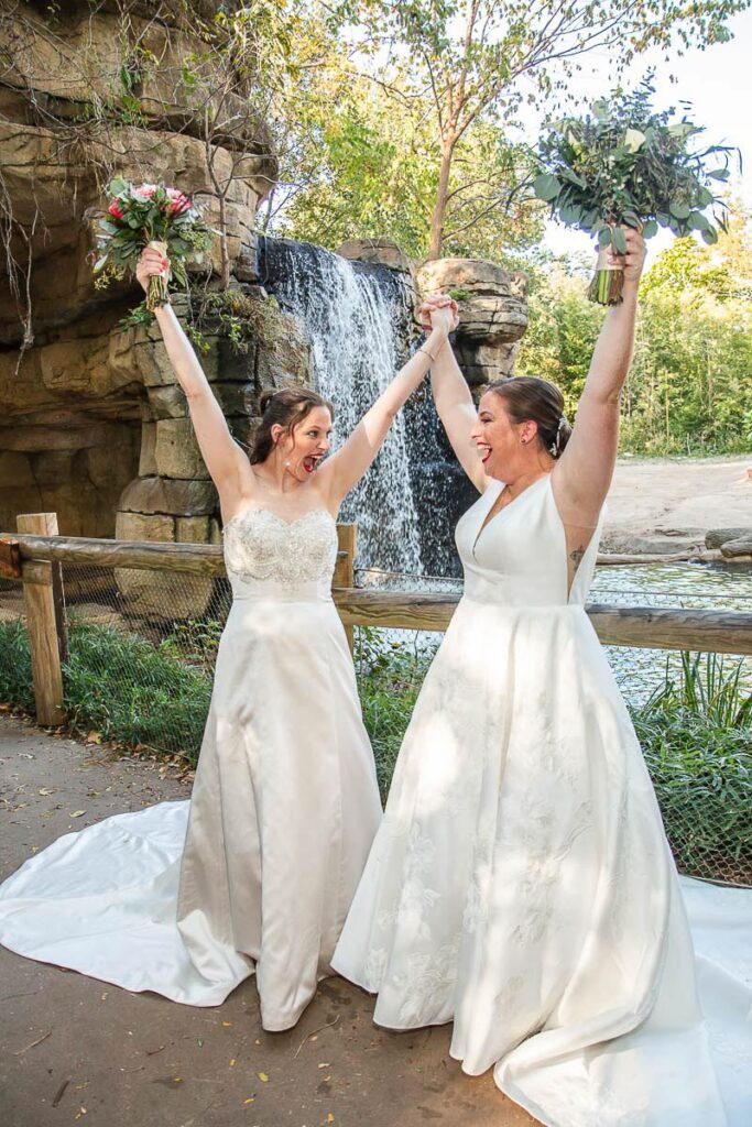 The brides raising their arms near a waterfall feature