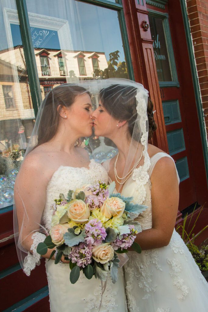 Two brides kissing each other under the veil