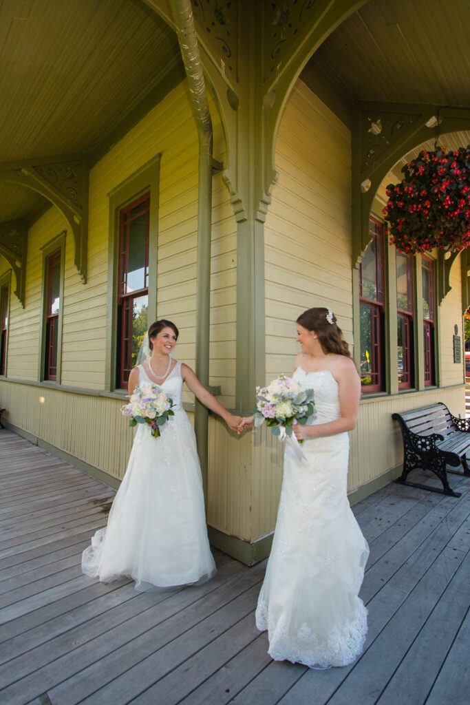 Two brides holding hands at a building’s corner