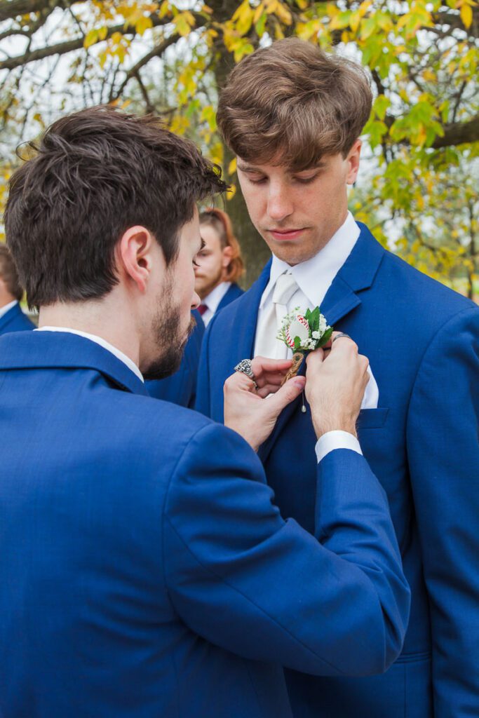 A groomsman places a boutonniere on Jonathan’s coat