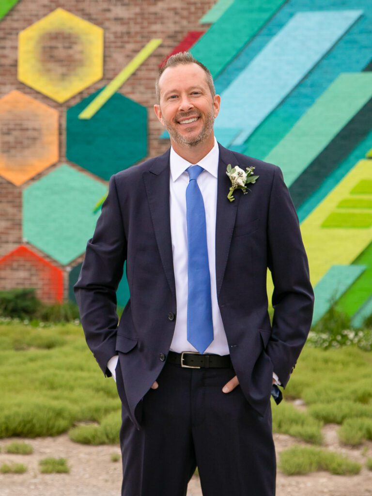 A groom smiling with a colorful brick wall behind him