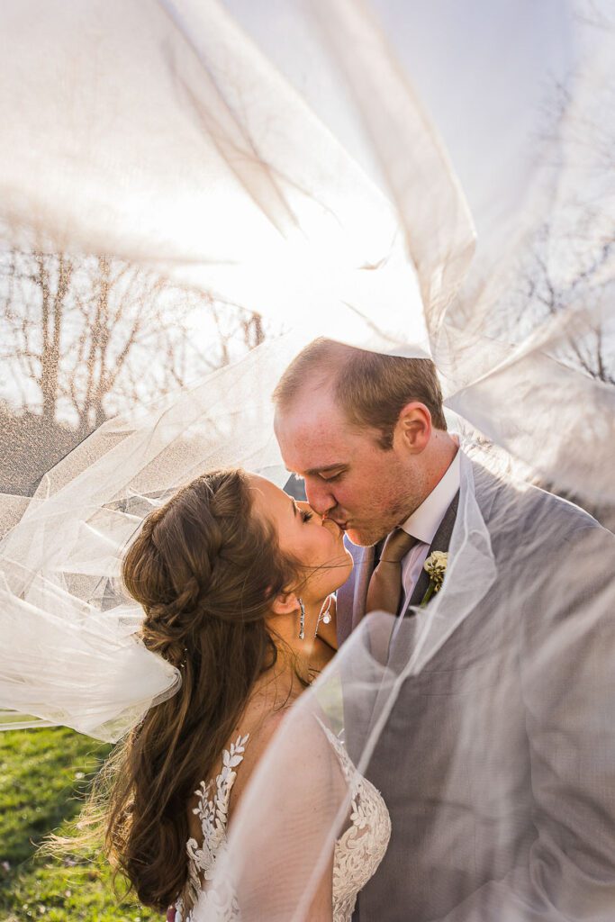 Bride and groom kissing each other under veil