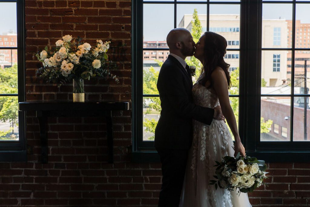 A close shot of Groom and bride standing and kissing along with a flower bouquet