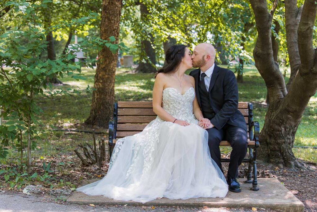 Bride and Groom sitting and kissing on a bench