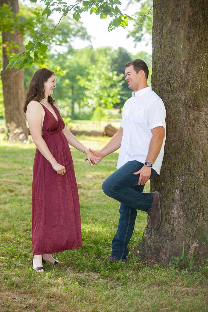 Husband leaning on tree and holding his wife's hand